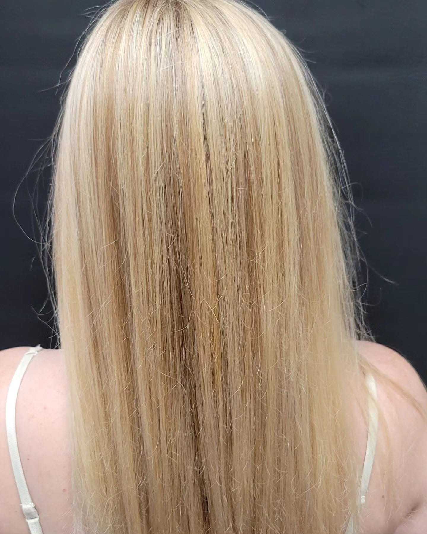 Blonde hair from behind, straightened and flowing, against a dark background.