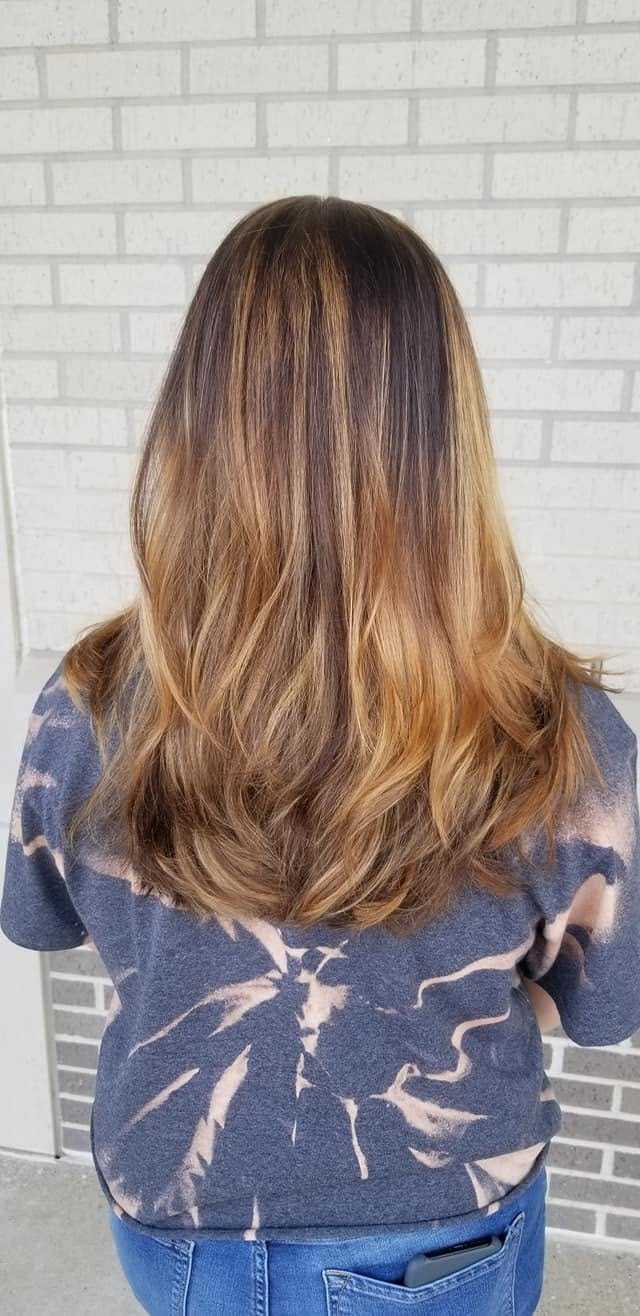 Back view of a person with long, layered brown hair against a brick wall.
