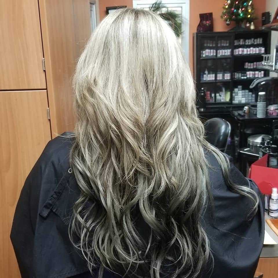 Blonde hair with dark roots styled in soft waves, seen from the back in a hair salon.