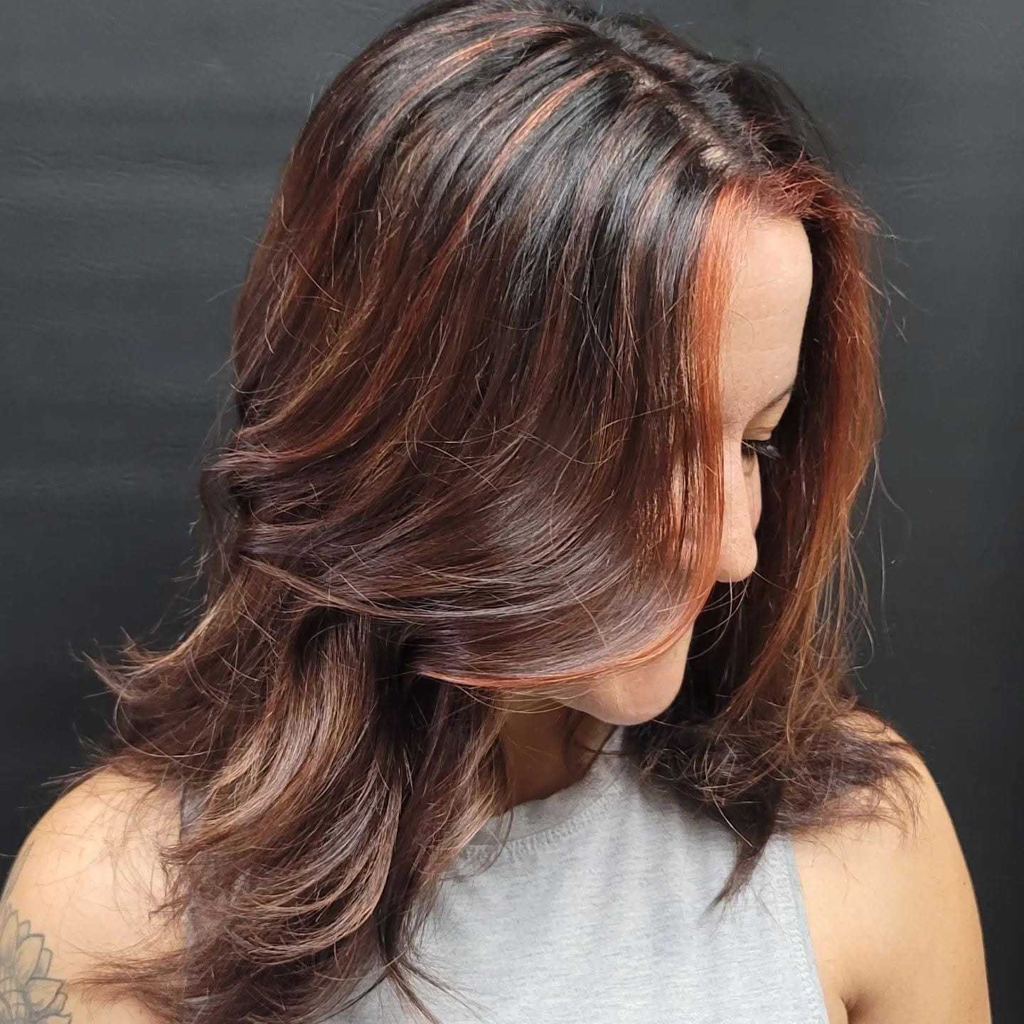 Medium brown hair with red highlights styled in soft waves.