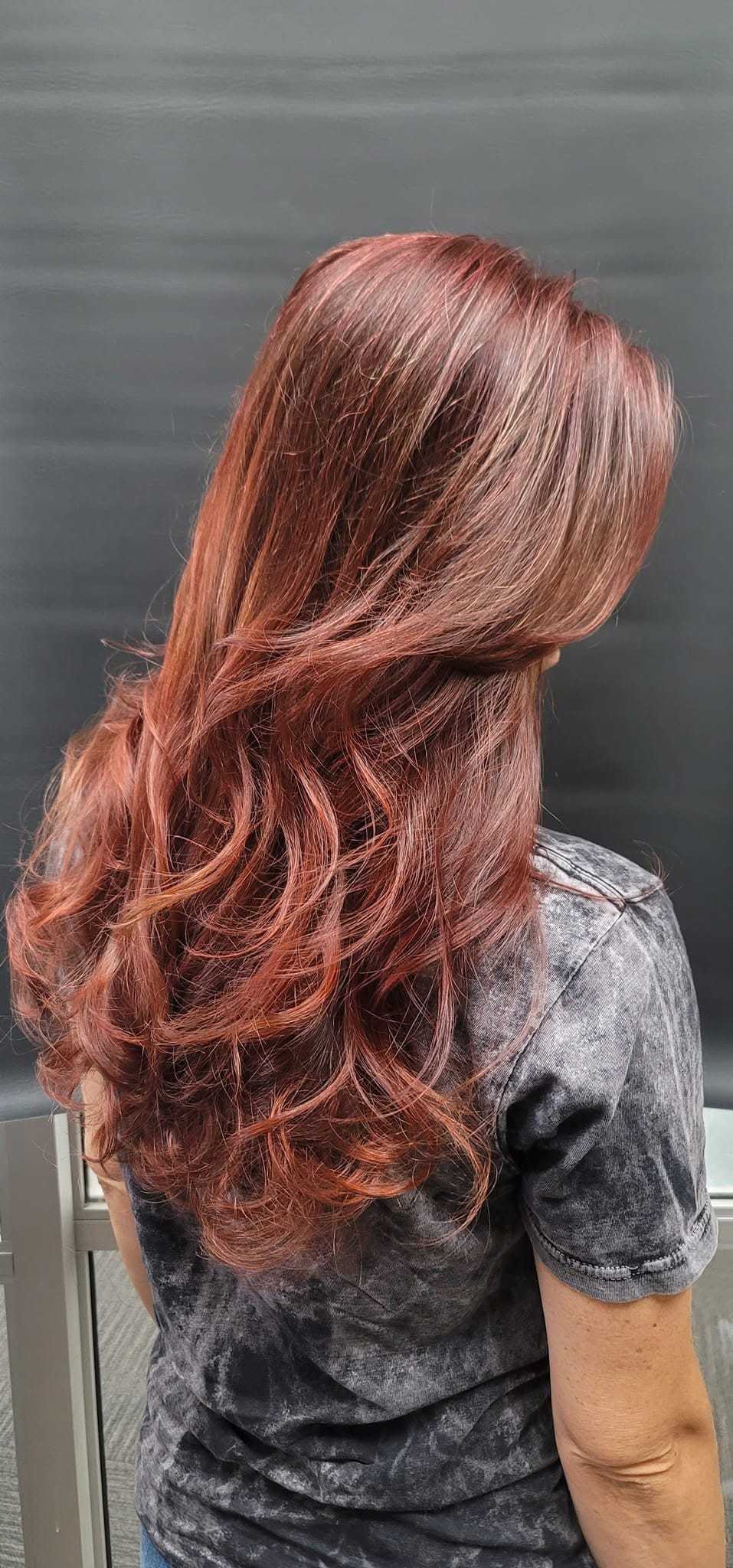 Woman with wavy, reddish-brown hair styled in soft curls, facing away.